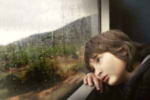 Sad boy looking out a rainy window before someone contacts a Child Abuse Lawyer San Francisco, CA to help him